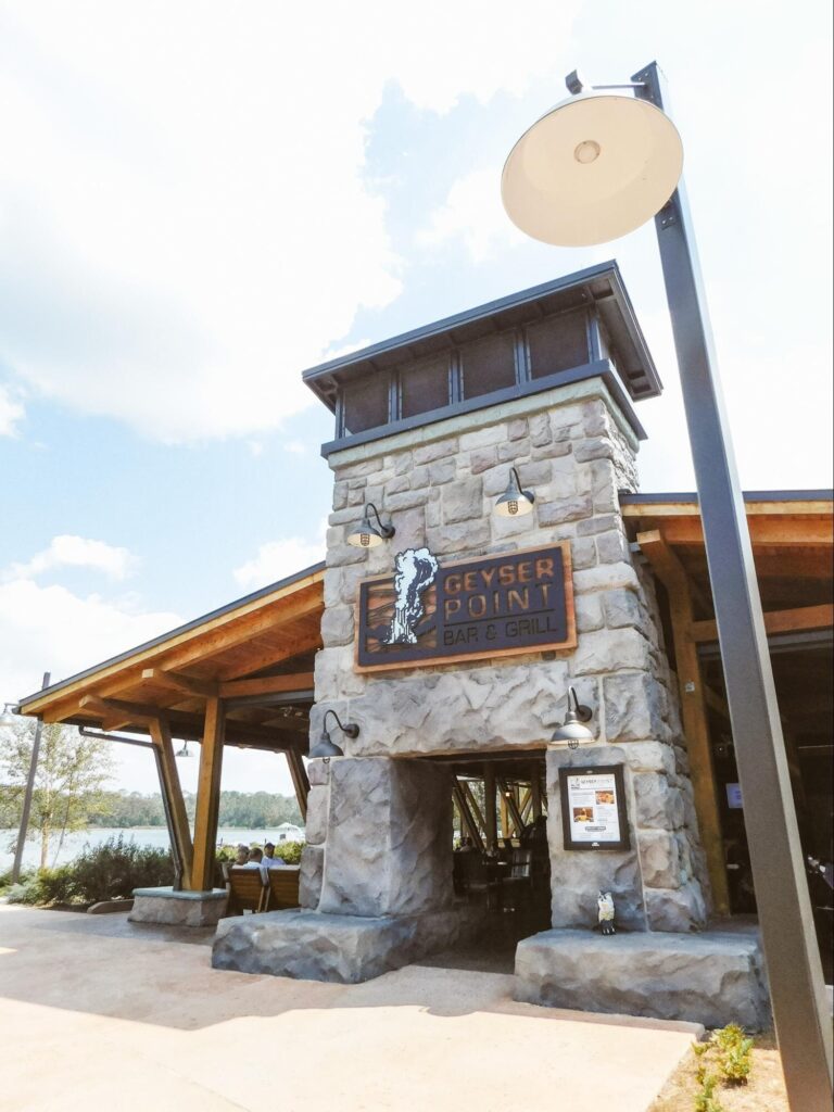 A one-story building made of wood with a stone brick entrance and a sign which reads "Geyser Point Bar and Grill." The building resembles a cabin.