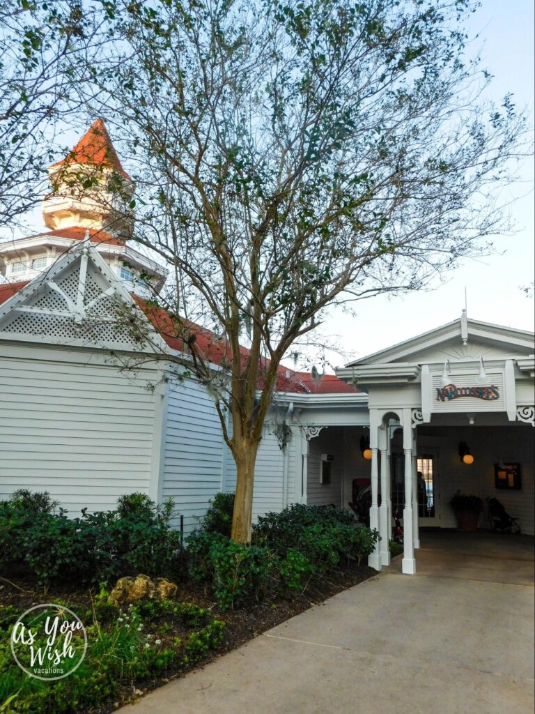 The entrance to Narcoossee, a building with off-white siding, white eaves with swirl motifs in the corners of archways, and a garden.