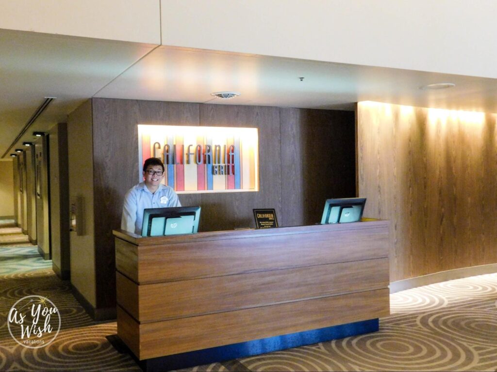 A waiter standing at a desk in front of the California Grill sign, smiling.