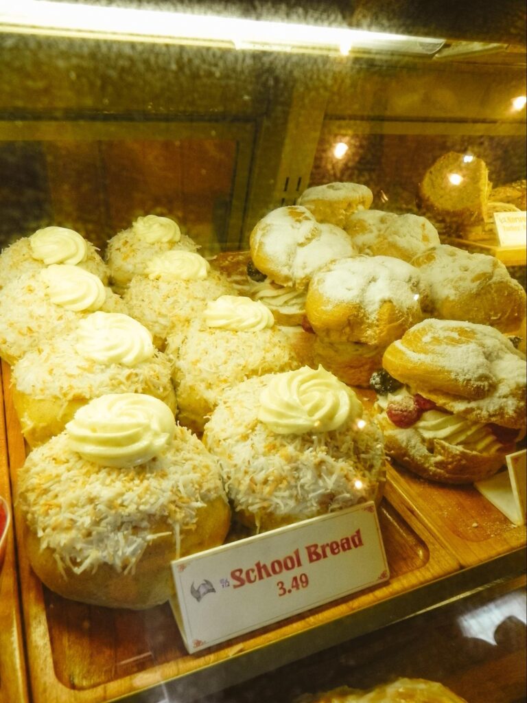 A bakery display labeled "school bread," fried dough filled with pastry cream and topped with coconut and a small swirl of frosting.