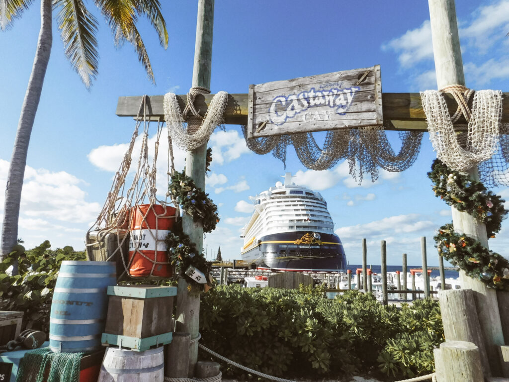 A wooden arch with a sign which reads "Castaway Cay" with a cruise ship visible in the background.